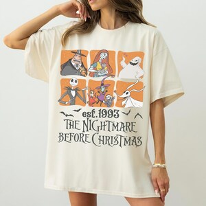 May include: Cream-coloured t-shirt with a graphic design from "The Nightmare Before Christmas." The design includes character illustrations in orange squares, the text "est. 1993," and the film's title in a stylized font.