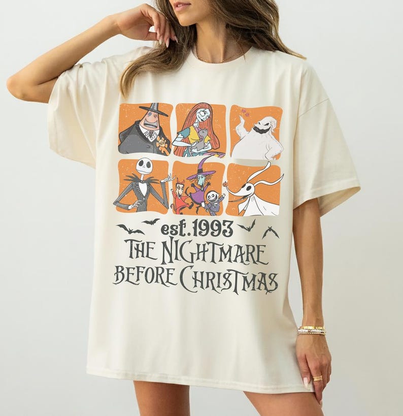 May include: Cream-coloured t-shirt with a graphic design from "The Nightmare Before Christmas." The design includes character illustrations in orange squares, the text "est. 1993," and the film's title in a stylized font.