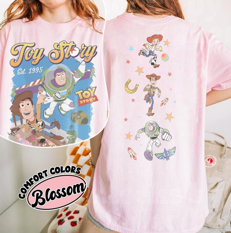 May include: Pink t-shirt featuring the Toy Story logo and characters. The front displays Buzz Lightyear, Woody, and the Toy Story logo. The back showcases Jessie, Woody, and Buzz Lightyear with stars and a horseshoe.
