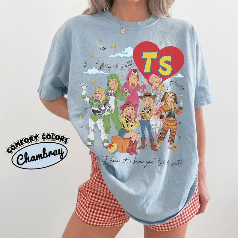 Puede incluir: Una camiseta de manga corta azul claro con un estampado gr&aacute;fico de siete personajes disfrazados inspirados en Toy Story. Un coraz&oacute;n rojo contiene el texto amarillo TS. Debajo de los personajes, el texto dice, I knew it, i krew you.