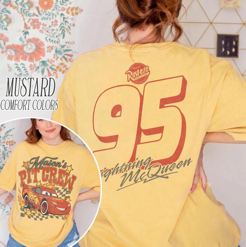 Op de afbeelding: Een mosterdgeel t-shirt met een groot rood nummer 95 en de tekst Rusteze en Lightning McQueen op de achterkant. De afbeelding op de voorkant toont een rode raceauto met het nummer 95, geblokte patronen, sterren en de tekst Mason's Pit Crew.