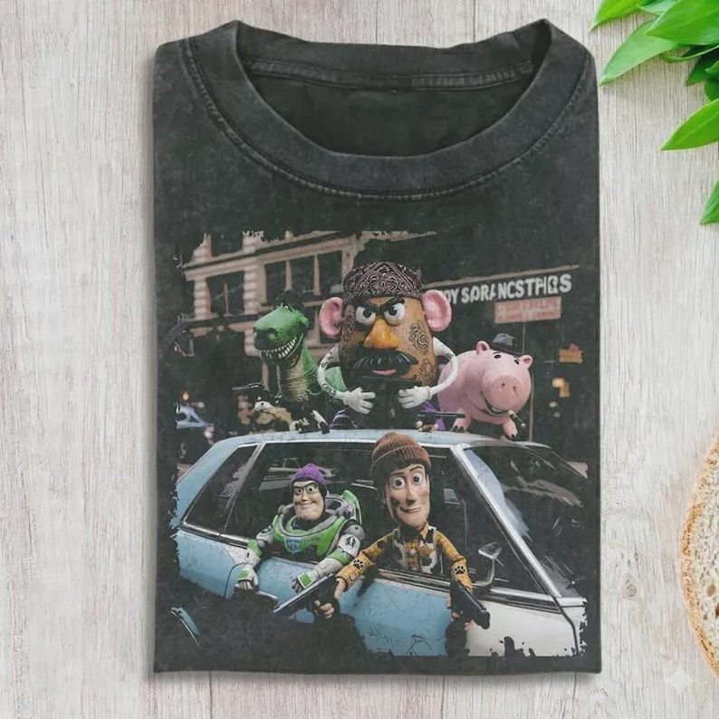 Puede incluir: Una camiseta gris carb&oacute;n con efecto lavado al &aacute;cido que presenta un estampado gr&aacute;fico de personajes de Toy Story, incluyendo al Sr. Patata, Rex, Hamm, Buzz Lightyear y Woody. Los personajes est&aacute;n situados alrededor de un coche azul claro.