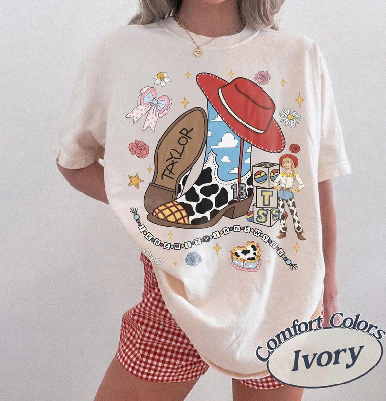 May include: An ivory t-shirt featuring a graphic print of a cowboy boot with a cow print pattern, a red cowboy hat, a small character figure, and stacked blocks with the letters BTS. The text TAYLOR and I KNEW IT I KNEW YOU are included.