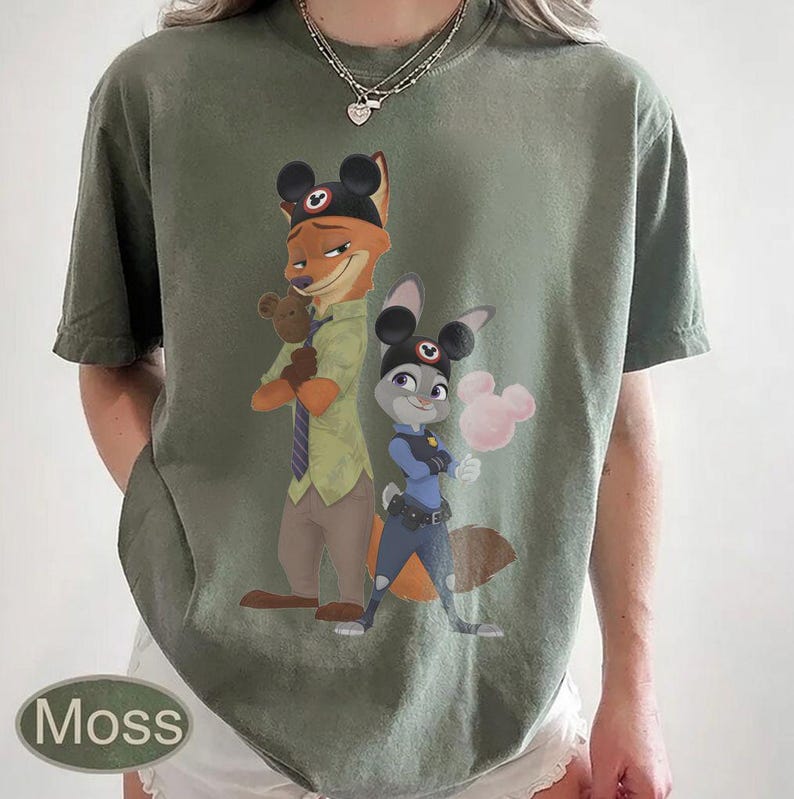 Pu&ograve; includere: T-shirt verde muschio con un'illustrazione a cartoni animati di Nick Wilde e Judy Hopps di Zootropolis, con orecchie di Topolino. Nick tiene un orsacchiotto e Judy uno zucchero filato rosa. La parola "Moss" &egrave; stampata in basso a sinistra.