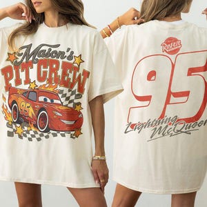 Op de afbeelding: Een off-white t-shirt met een vooropdruk van een rode raceauto met de tekst Mason's PIT CREW en gele sterren. De achterkant van het shirt toont een groot rood nummer 95, het Rust-eze logo en de tekst Lightning McQueen in een cursief lettertype.