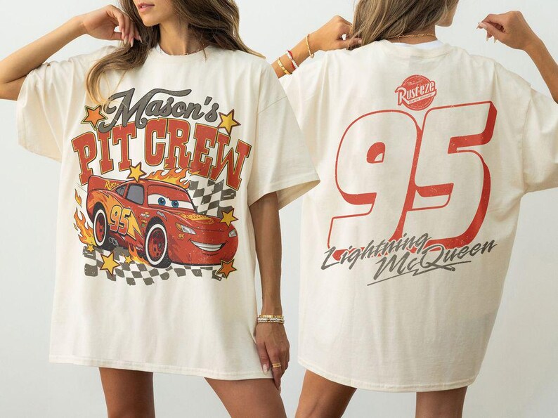 Op de afbeelding: Een off-white t-shirt met een vooropdruk van een rode raceauto met de tekst Mason's PIT CREW en gele sterren. De achterkant van het shirt toont een groot rood nummer 95, het Rust-eze logo en de tekst Lightning McQueen in een cursief lettertype.