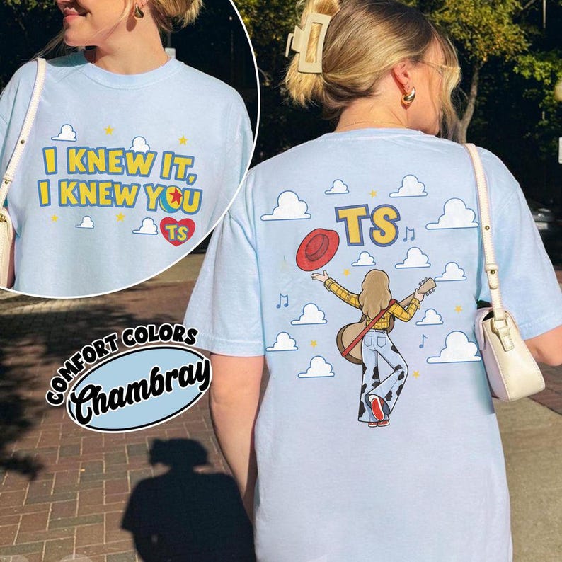 May include: A light blue t-shirt featuring a graphic on the front that reads I KNEW IT, I KNEW YOU with a heart and TS. The back graphic shows a person with a guitar, a red hat, and the text TS against a background of clouds and stars.