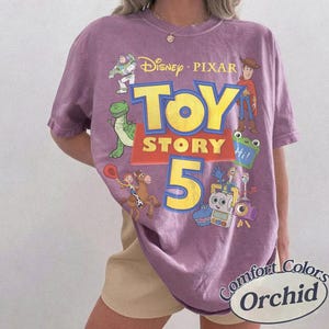 Puede incluir: Una camiseta morada de manga corta con un gran estampado gr&aacute;fico que incluye el texto Disney Pixar Toy Story 5. El dise&ntilde;o muestra ilustraciones de Buzz Lightyear, Woody, Rex, Jessie, Bullseye y otros personajes. Tiene cuello redondo.