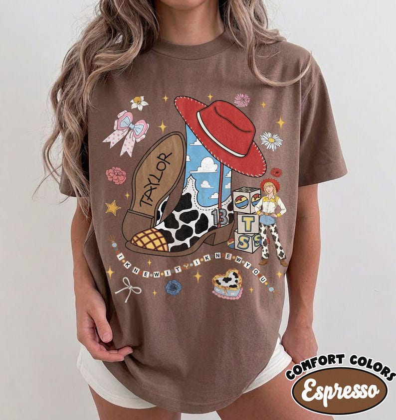 May include: A brown t-shirt featuring a graphic print of a cowboy boot with a cow print pattern, a red cowboy hat, a cartoon character, and alphabet blocks. The text "TAYLOR" and "I KNEW IT I KNEW YOU" are printed alongside stars, flowers, and a bow.