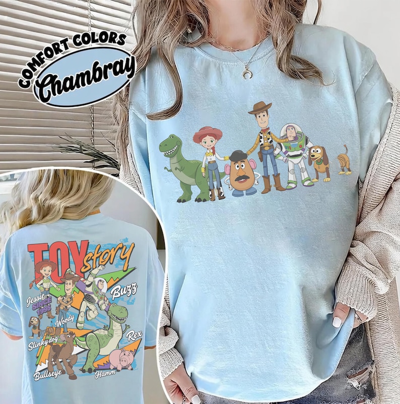 Może przedstawiać: Jasnoniebieska koszulka chambray z grafiką postaci z Toy Story. Prz&oacute;d koszulki przedstawia postacie w rzędzie, a tył ma logo Toy Story i więcej postaci. Koszulka ma słowa "Comfort Colors" i "Chambray" w lewym g&oacute;rnym rogu.