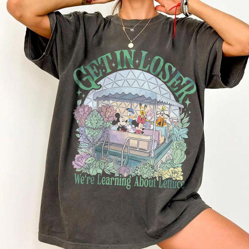 Pode incluir: Camiseta cinza escuro com um gr&aacute;fico colorido de um passeio com personagens de desenhos animados e o texto "GET IN LOSER We're Learning About Lettuce". O design inclui Mickey Mouse, Pato Donald e Pateta.