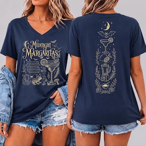 May include: A navy blue V-neck t-shirt featuring gold graphic prints. The front displays the text Midnight Margaritas with a cocktail glass, a frog, and small icons. The back shows a vertical arrangement of a crescent moon, bat, cocktail, lime, blender, and bowl.