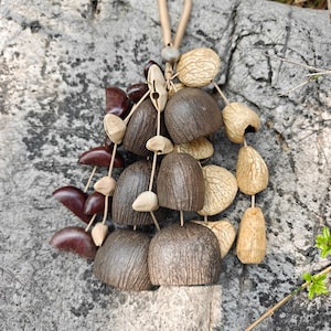 Puede incluir: Un collar artesanal con elementos naturales. Presenta un conjunto de formas org&aacute;nicas marrones, beige y marr&oacute;n rojizo, ensartadas en un cord&oacute;n natural. El dise&ntilde;o incorpora diversas texturas y formas, creando una est&eacute;tica &uacute;nica y terrenal.