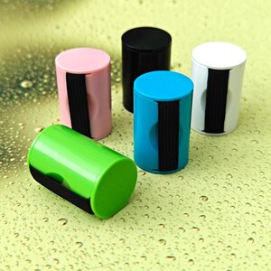 May include: Five cylindrical plastic containers in pink, black, blue, white, and green. Each container features a vertical black elastic band wrapped around its centre. The containers have flat circular tops and smooth, solid-coloured surfaces.