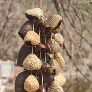 Puede incluir: Un carill&oacute;n de viento colgante con elementos naturales. Incluye piezas en forma de campana y vaina en tonos marrones y beige, unidas con cuerda. El dise&ntilde;o evoca una est&eacute;tica r&uacute;stica o bohemia, ideal para exteriores.