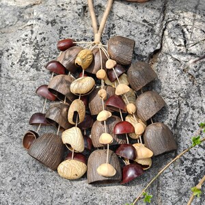 Puede incluir: Un collar artesanal hecho con elementos naturales. Presenta un conjunto de cuentas de madera y vainas de semillas en tonos marr&oacute;n, beige y burdeos, ensartadas con un cord&oacute;n natural, creando un dise&ntilde;o &uacute;nico y org&aacute;nico.