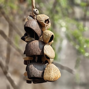 Puede incluir: Un m&oacute;vil de viento colgante compuesto por materiales naturales y texturizados. El m&oacute;vil presenta una serie de elementos en forma de campana en tonos marr&oacute;n, beige y tostado, suspendidos de un cord&oacute;n tejido. El dise&ntilde;o incorpora diversas formas y texturas org&aacute;nicas.