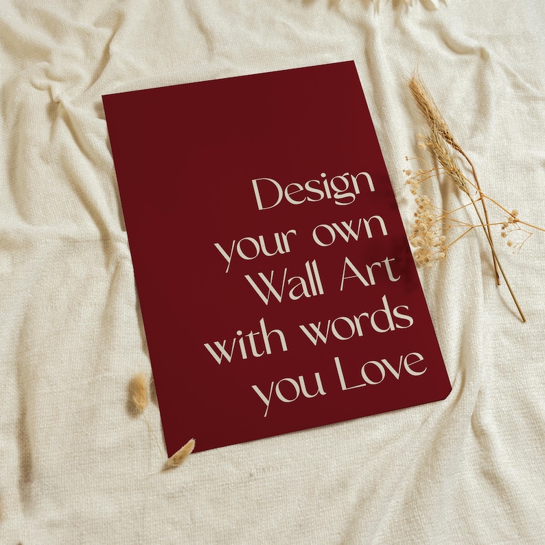 Może przedstawiać: Prostokątny ciemnoczerwony wydruk z białym napisem: Design your own Wall Art with words you Love. Wydruk umieszczono na teksturowanej powierzchni z tkaniny w kolorze złamanej bieli obok małego pęczka suszonych beżowych łodyg pszenicy.