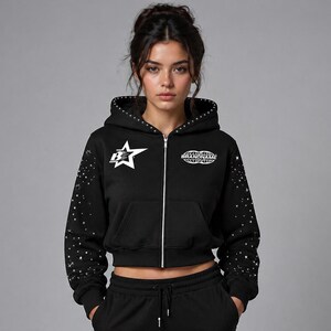 May include: Black zip-up hoodie with a white star graphic and the text "BRANDNAME". The hoodie features a studded design on the hood and sleeves. The model is wearing a matching black sweat suit.