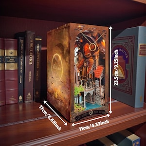 May include: A wooden Lord of the Rings-themed book nook, 9.25 inches tall, 6.69 inches wide, and 4.33 inches deep. The interior features a detailed miniature scene with a bridge, buildings, and a ring pendant. The book nook is displayed on a bookshelf.