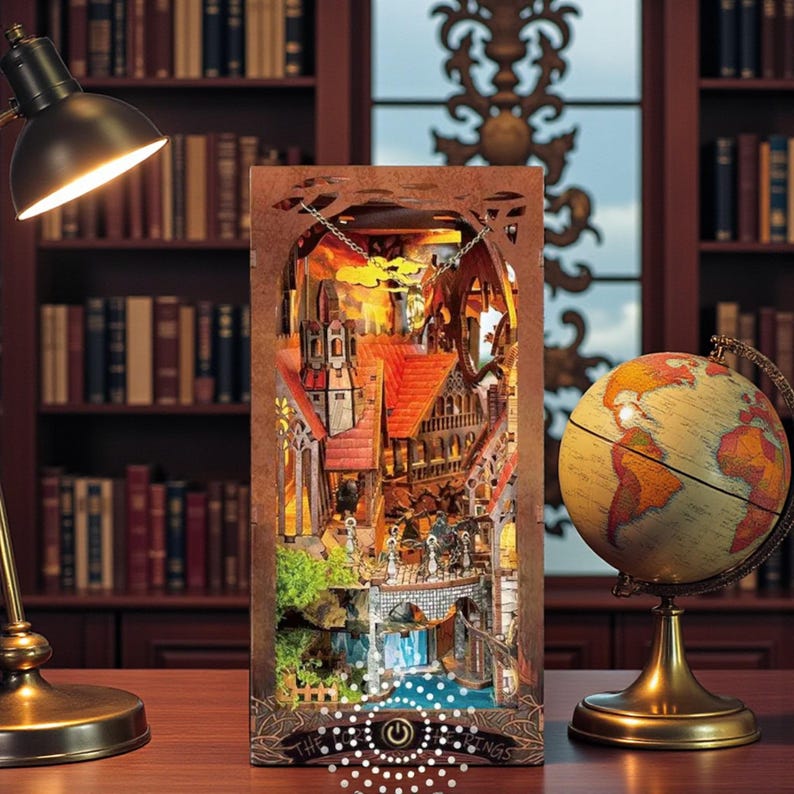 May include: A detailed, illuminated wooden diorama depicting a European town scene with red-tiled roofs, bridges, and a waterfall. The diorama is lit from within, creating a warm glow. A globe and lamp are on the table.