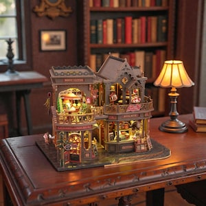 Pu&ograve; includere: Modello in miniatura dettagliato di un edificio a due piani con una caffetteria e una libreria. Il modello &egrave; marrone e grigio con intricati dettagli architettonici, illuminato dall'interno. Le parole "MAGIC COFFEE" e "BOOK SHOP" sono visibili. Una piccola lampada &egrave; vicina.