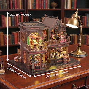 Pu&ograve; includere: Un modello in miniatura dettagliato di una caffetteria e libreria, alto 20,3 cm e largo 25,6 cm. Il modello presenta intricati dettagli architettonici, con le parole "MAGIC COFFEE", "WONDERFUL COFFEE HOUSE" e "BOOK SHOP" visibili.