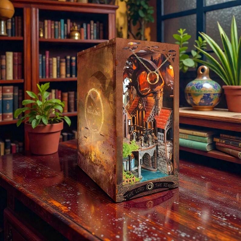 May include: A detailed, laser-cut wooden book-shaped lamp featuring a scene from The Lord of the Rings. The lamp has a warm, inviting glow, with intricate architectural details and a golden ring pendant. The book is displayed on a wooden table.