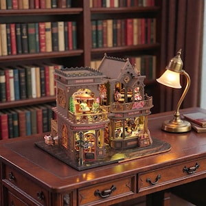 Pu&ograve; includere: Un modello in miniatura dettagliato di una caffetteria e libreria, con una calda illuminazione interna. Il modello presenta intricati dettagli architettonici, tra cui balconi e insegne che recitano "Magic Coffee" e "Book Shop". Il modello &egrave; su una scrivania di legno con una lampada in ottone.