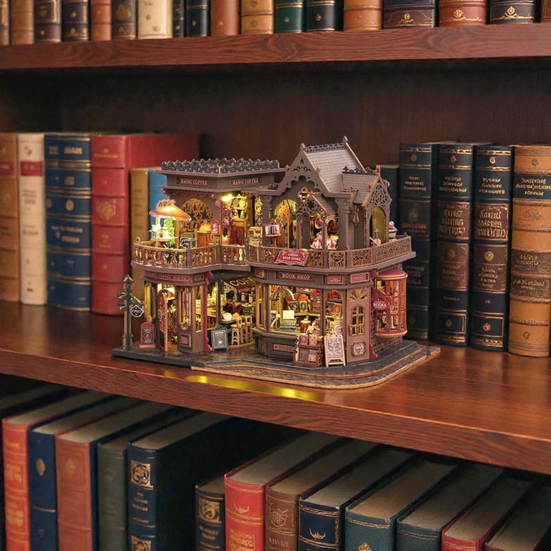 Pu&ograve; includere: Modello in miniatura dettagliato di una libreria e caffetteria, con calda illuminazione interna. La struttura a due piani presenta intricati dettagli architettonici, tra cui balconi e tende da sole. Il modello &egrave; esposto su una mensola di legno circondata da libri antichi.