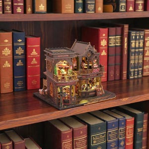 Pu&ograve; includere: Un modello in miniatura dettagliato di un edificio a due piani con le scritte "MAGIC COFFEE" e "BOOK SHOP" visibili. Il modello &egrave; marrone con intricati dettagli architettonici ed &egrave; illuminato da luci interne. Si trova su una mensola di legno circondata da libri.
