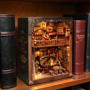 May include: A miniature diorama of a tavern, illuminated with warm lighting, nestled within a decorative book. The scene features a bar, tables, and figures, with the text "Welcome to Old Times Tavern" on the book's spine. The diorama is on a wooden shelf.