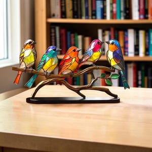 Puede incluir: Un adorno de mesa decorativo que presenta cinco pájaros coloridos elaborados en un estilo de vidrieras, posados sobre una rama de metal marrón. Cada pájaro muestra una combinación única de tonos vibrantes como rojo, amarillo, azul y verde.