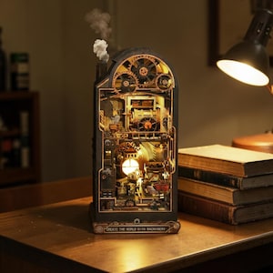May include: A detailed, illuminated steampunk model with visible gears, pipes, and internal mechanisms. The model is black and gold, with a chimney emitting a wisp of smoke. The base reads "CREATE THE WORLD WITH MACHINERY".