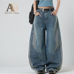 May include: Blue denim wide-leg jeans with white stripes down the sides. The jeans have a high waist and a relaxed fit. The image also shows a black belt and a black backpack. The brand name "AbieDazzling" is visible in the upper left corner.