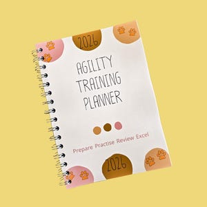Op de afbeelding: Een spiraalgebonden agility trainingsplanner voor 2026. De cover is wit met de woorden "Agility Training Planner" in het zwart. Het heeft pootafdrukken en het jaar 2026 in bruine en roze cirkels. De tekst "Prepare Practice Review Excel" is ook opgenomen.