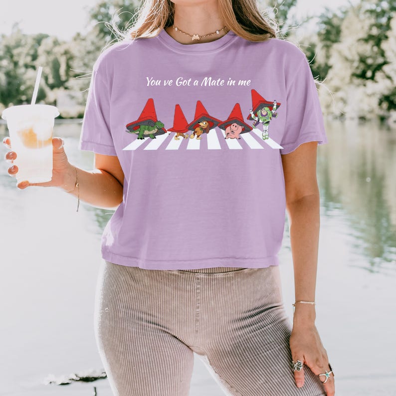 May include: A lilac-colored t-shirt with the text "You've Got a Mate in me" above a graphic of four cartoon characters crossing a white crosswalk. The characters are wearing red hats.