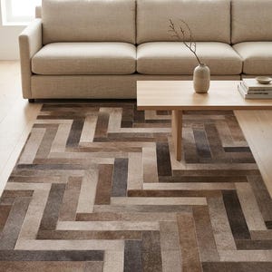 May include: A rectangular area rug featuring a multi-tonal brown and gray herringbone pattern composed of individual rectangular patches. The rug displays a variety of earthy shades arranged in a geometric, interlocking weave design across its surface.