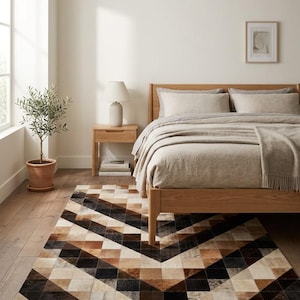 May include: A rectangular area rug featuring a geometric pattern of triangles in shades of black, brown, tan, and cream. The rug is constructed from stitched panels of hide, creating a textured surface with a repeating chevron-like design.