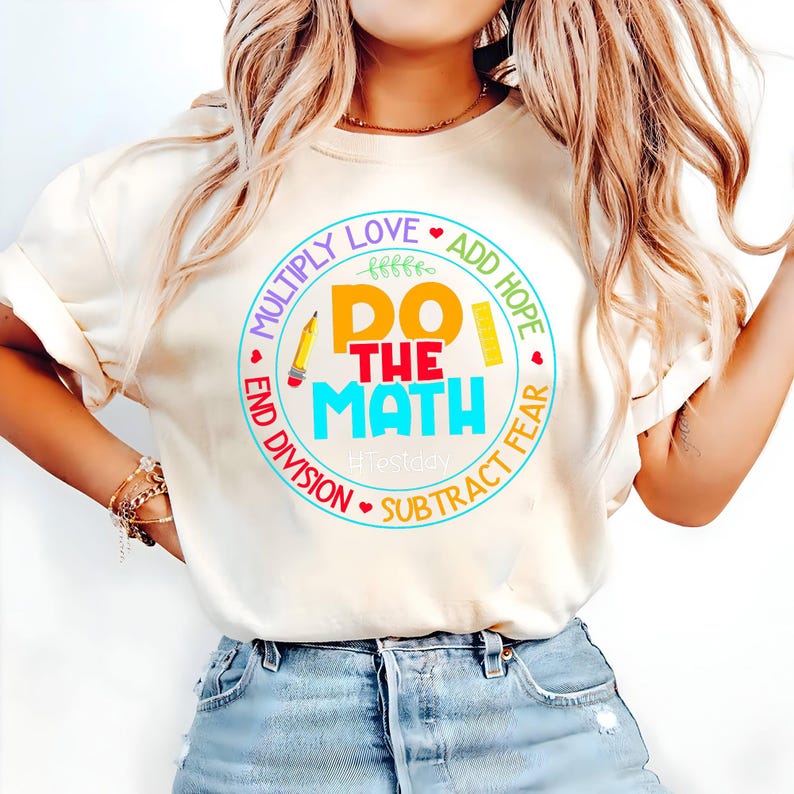 May include: Cream-colored t-shirt with a colorful graphic that says "Do The Math" in a circle with the words "Multiply Love, Add Hope, Subtract Fear, End Division". A pencil and ruler are also in the design.