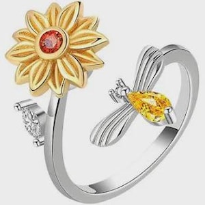 May include: A silver-toned ring featuring a sunflower with gold-colored petals and a red center stone. A bee with a yellow gemstone body and silver wings is on the ring band. A small, clear stone is also on the band.