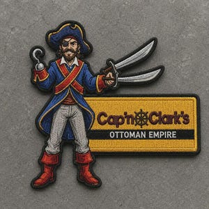 Puede incluir: Un parche bordado que muestra a un pirata con abrigo azul, faja roja y parche en el ojo, sosteniendo un garfio y dos espadas. Junto al personaje hay un letrero rectangular amarillo con el texto negro Cap'n Clark's OTTOMAN EMPIRE.