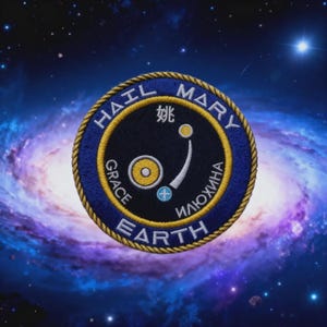 May include: A circular embroidered patch with a dark blue border and gold rope-style trim. The centre features a black field with a yellow sun, a light blue planet with a white cross, and a white arc. Text includes HAIL MARY, GRACE, EARTH, and Russian and Chinese characters.