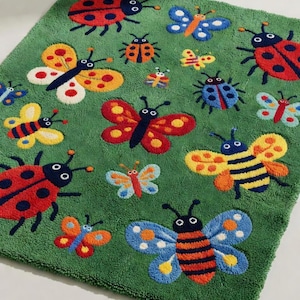 Può includere: Un tappeto rettangolare verde trapuntato con un motivo ripetuto di insetti colorati, tra cui coccinelle rosse, api gialle e arancioni e varie farfalle nelle tonalità del blu, giallo, rosso e arancione con dettagli neri su tutto il design.