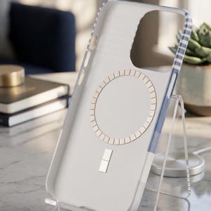 May include: A clear phone case with a blue and white striped border. The interior features a circular magnetic ring array and a small rectangular alignment magnet at the bottom, designed for wireless charging compatibility.