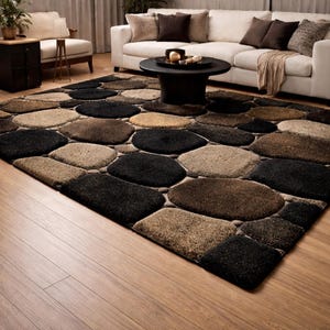 Puede incluir: Una alfombra rectangular grande con un diseño de guijarros. La alfombra presenta un patrón de formas redondeadas de varios tamaños en tonos de negro, marrón y beige. La alfombra está colocada sobre un suelo de madera, con un sofá blanco y una mesa de centro en el fondo.