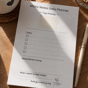 Może przedstawiać: Biały notatnik do planowania dnia z czarnym tekstem zatytułowany Sticky Notes Daily Planner. Zawiera sekcje Top Priority, listę pięciu pól wyboru dla Tasks, obszar Notes/Brain Dump oraz sekcję How I want to feel today.