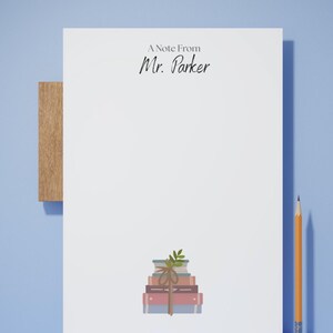 Peut inclure: Un bloc-notes blanc avec le texte "A Note From Mr. Parker" en écriture noire. Une pile de livres attachés avec de la ficelle et une brindille de feuilles en bas. Un crayon est sur le côté droit.