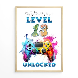 May include: A framed print with a colorful design. The artwork features a game controller, the words "Happy Birthday to you! LEVEL 13 UNLOCKED," and a splash of vibrant colors. The number 13 is stylized with money-themed graphics.