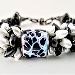 May include: Black and white beaded bracelet with a black and white patterned glass bead in the center.
